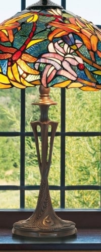 Lampe Tiffany colorée avec abat-jour en motifs floraux, base brune et décor détaillé sur table près d’une fenêtre.