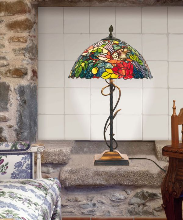 Lampe Tiffany colorée au design mosaïque, posée sur une veille table en pierre dans une pièce décorée rustique.