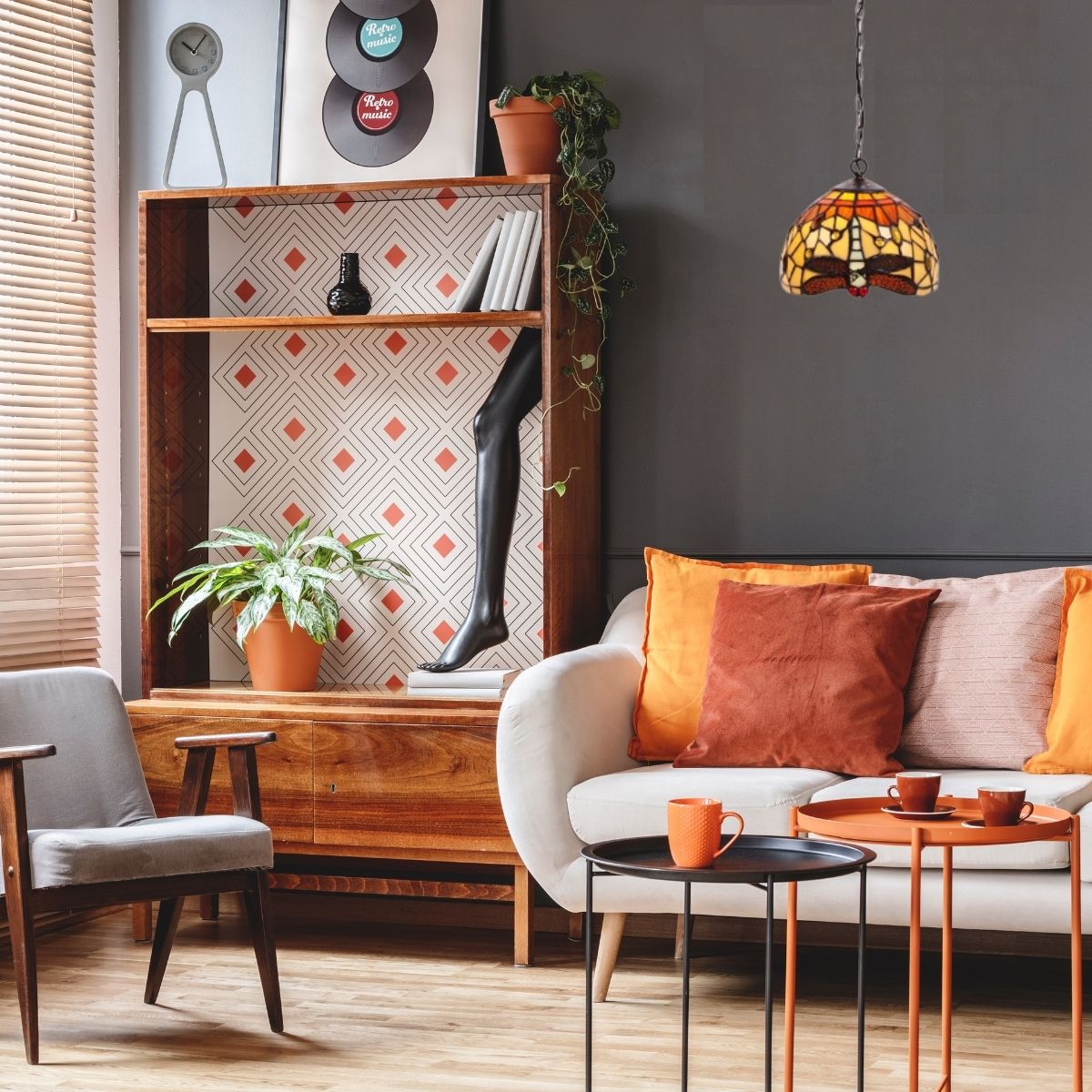 Décoration salon mélange ancien et moderne: canapé clair avec coussins orange, tables basses noires et orange, étagère vintage, plante en pot, lampe tiffany et affiches rétro.