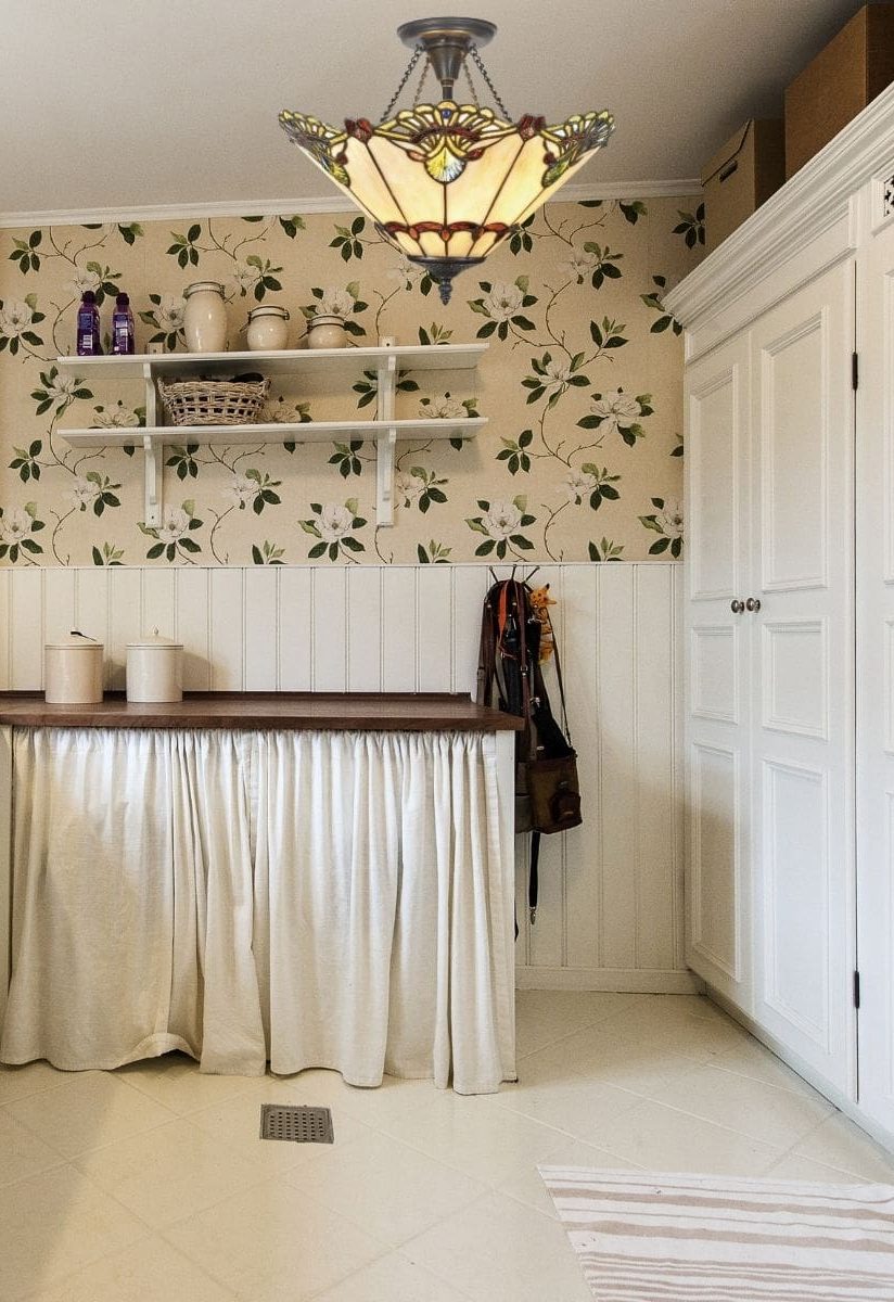 Lustre en plumes décoratif suspendu au-dessus d’un comptoir, dans une cuisine à papier peint floral et rangements blancs.