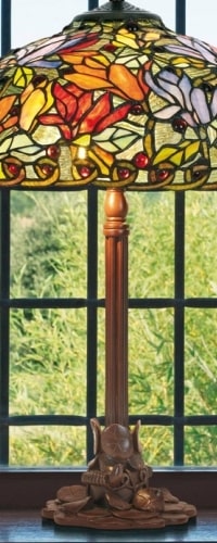 Lampe Tiffany avec abat-jour coloré en verre coloré et socle en bois posé près d’une fenêtre.