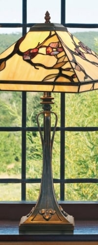 Lampe Tiffany avec abat-jour en pierre colorée sur une table devant une fenêtre.