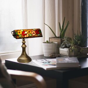Lampe de style Tiffany avec abat-jour coloré sur un bureau près de plantes et de magazines.