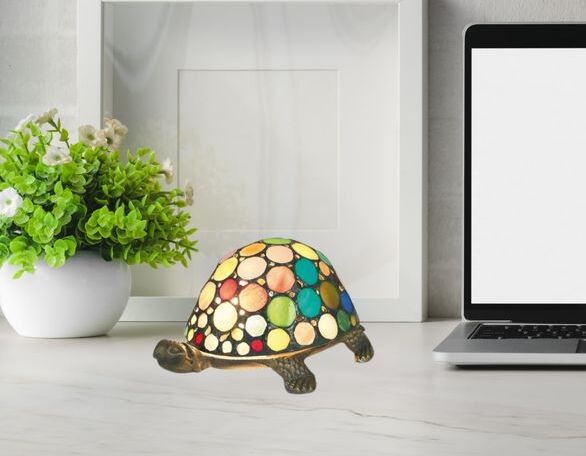 Lampe Tiffany colorée en forme de tortue posée sur une table près d’un cadre et d’un ordinateur portable.