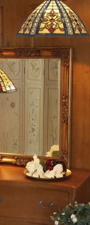 Miroir orné posé sur une commode en bois avec des abat-jours Tiffany et des éléments décoratifs sur le plateau.