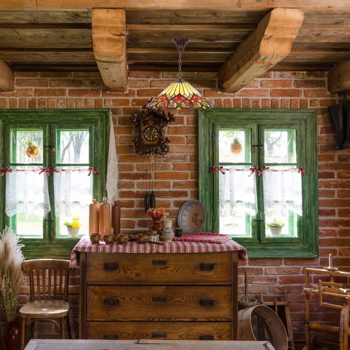 Pendant lumineux art déco suspendu au-dessus d'une table rustique dans une cuisine au mur de briques et fenêtres vertes.