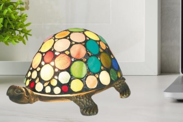 Petite lampe Tiffany en forme de tortue avec un abat-jour coloré composé de cercles multicolores sur fond noir posé sur une