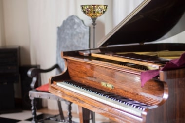 Piano droit en bois posé dans une pièce décorée avec des meubles et textiles visibles autour.
